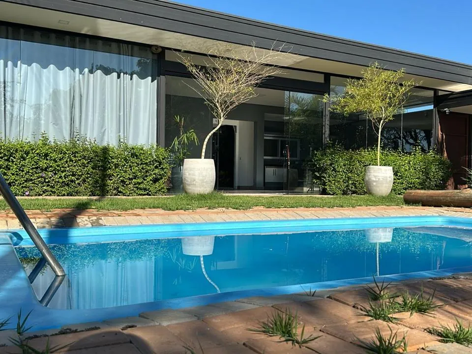 Piscina com deck e jardim ao lado de residência térrea envidraçada